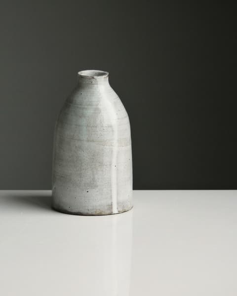 Grey speckled bottle vase on a white shelf against a dark wall