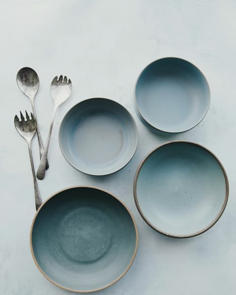 Four pale blue stoneware bowls with spoons on a white table