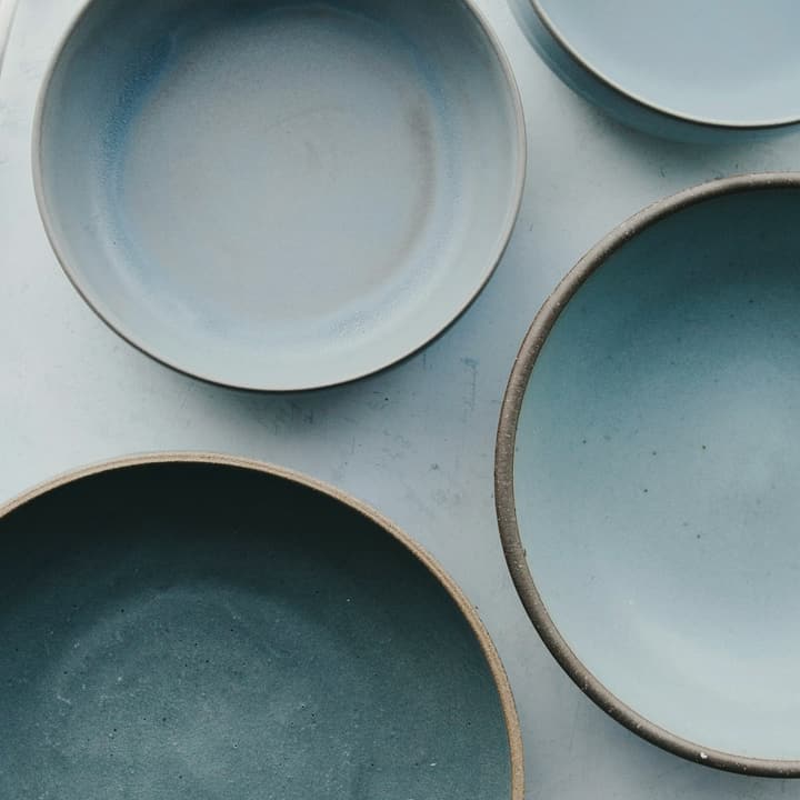 Four pale blue stoneware bowls with spoons on a white table, detail of the glaze