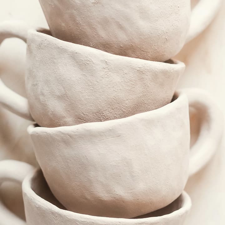 Three blush-pink cups stacked on a linen surface, detail of the glaze
