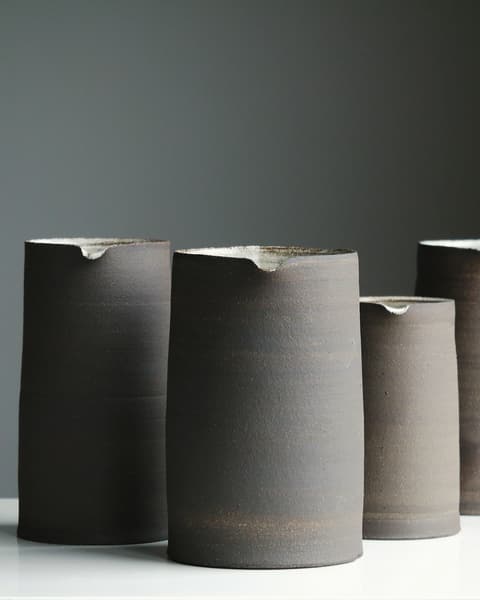 Three tall charcoal-grey cylinder vases on a white surface