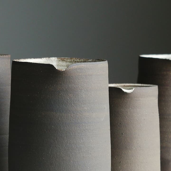 Three tall charcoal-grey cylinder vases on a white surface, detail of the glaze