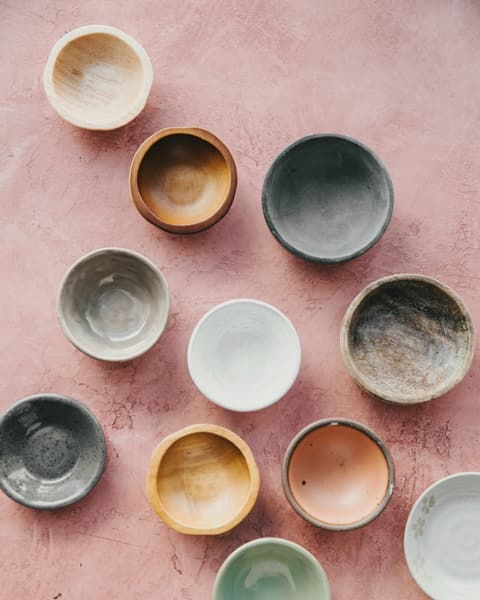 Nine small bowls in ochre, grey, white and pink glazes seen from above