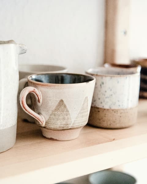 Two cream stoneware mugs on a wooden shelf
