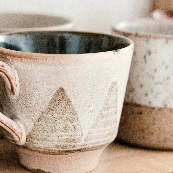 Two cream stoneware mugs on a wooden shelf, detail of the glaze