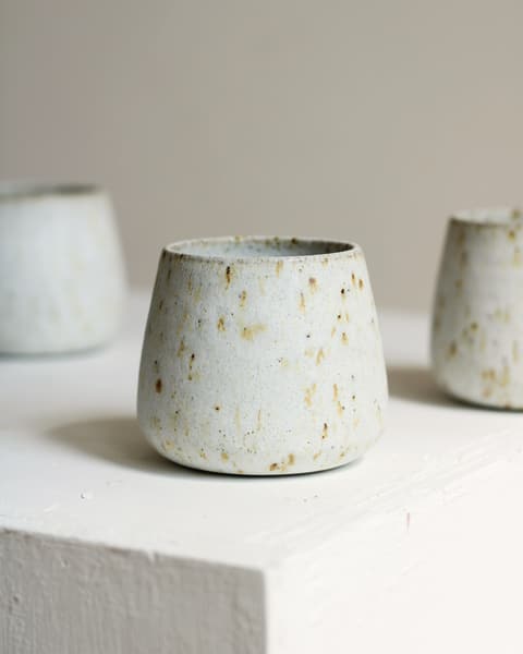 White tumbler with gold flecks on a white plinth