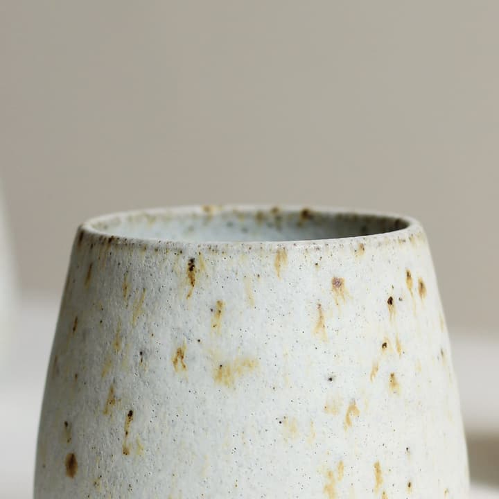White tumbler with gold flecks on a white plinth, detail of the glaze