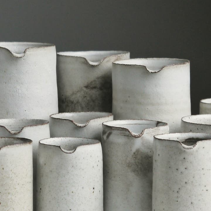 Six chalk-white stoneware tumblers grouped together, detail of the glaze